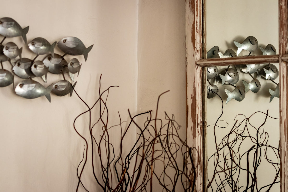 A mirror sitting next to a wall with a bunch of metal birds on it