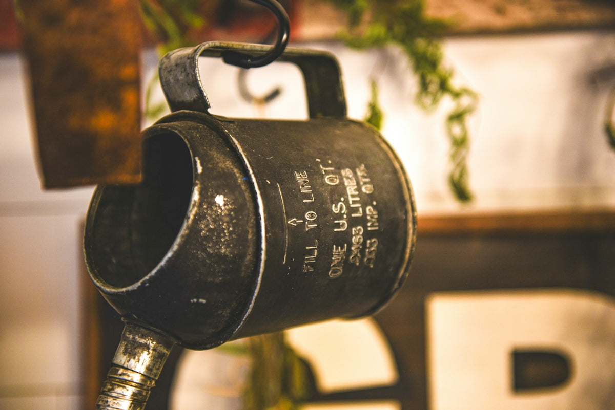 A vintage black metal oil can with measurement markings hanging from a hook