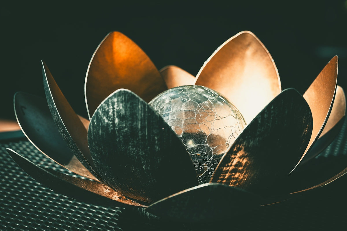 A metallic lotus flower sculpture with a cracked glass sphere
