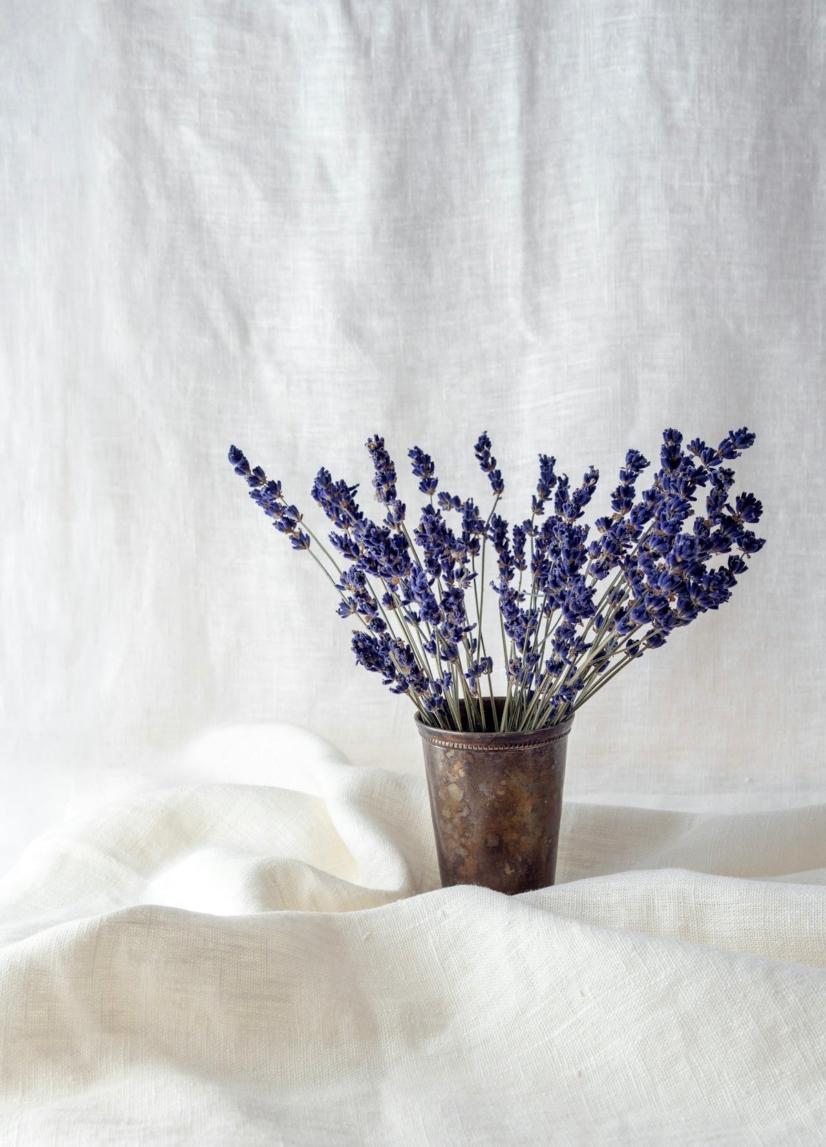 A bouquet of dried lavender in a tarnished metal cup on white linen