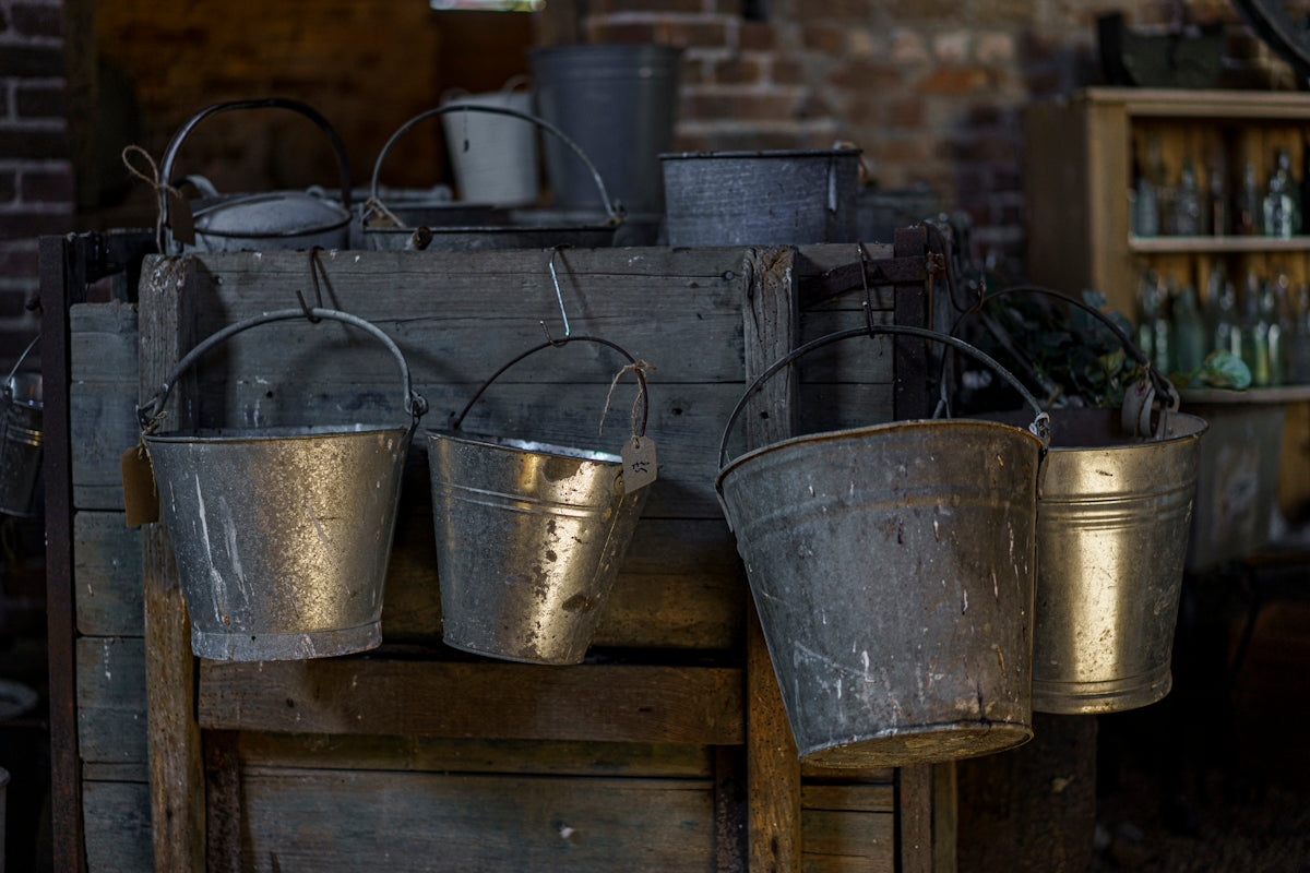 Galvanized metal buckets hanging from a rustic wooden crate in a dim barn