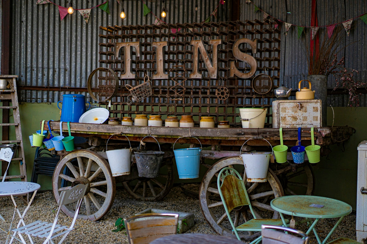 A rustic wooden cart displaying vintage tins and colorful buckets in a barn
