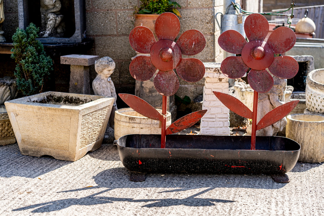 Two red metal flower sculptures in a black planter on a concrete patio