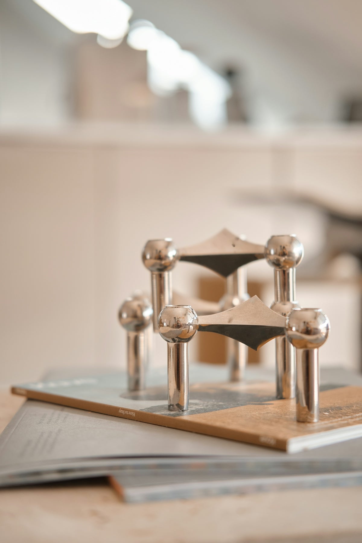 A modular silver metal candle holder on a book in a bright room