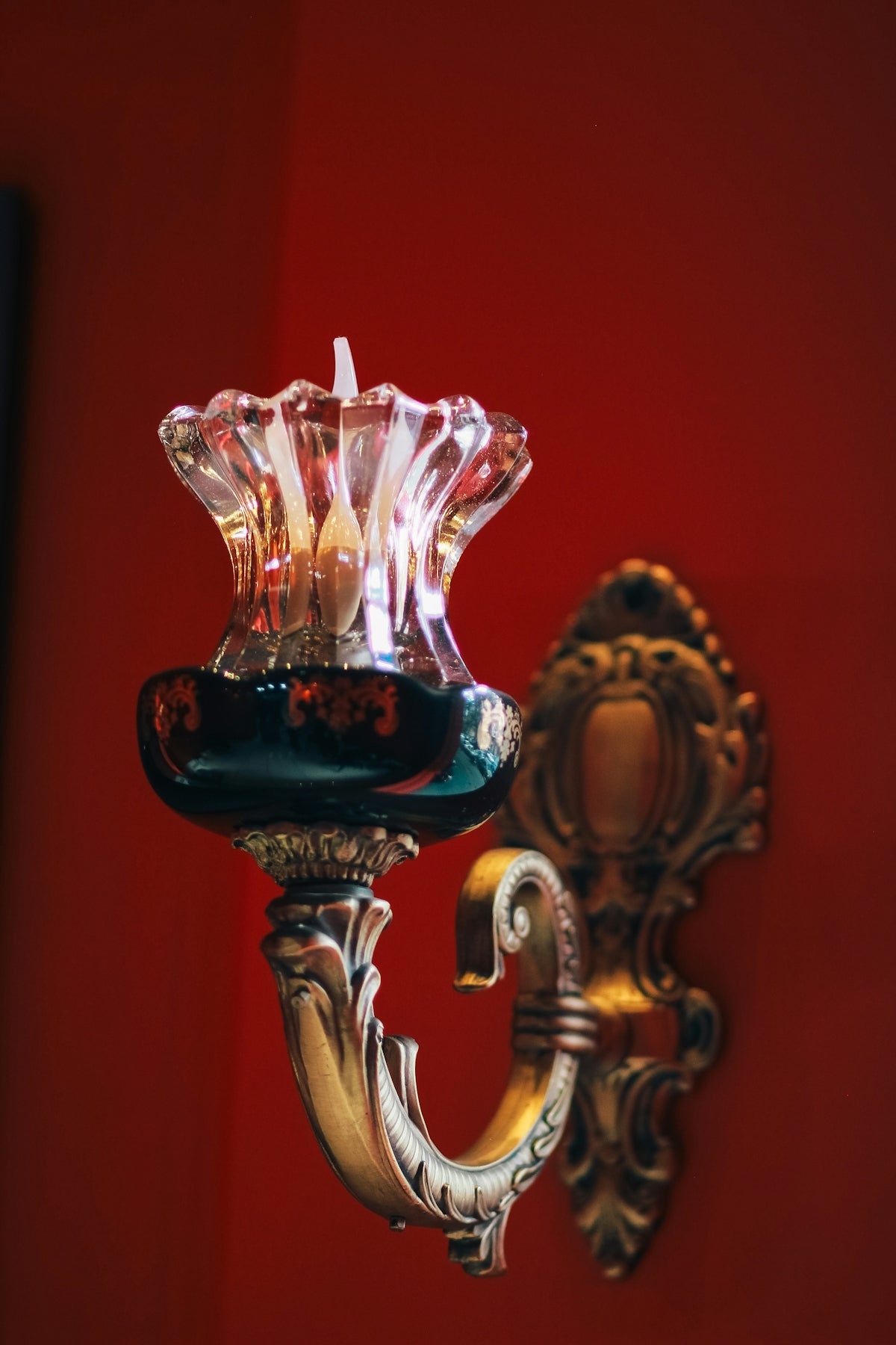 A decorative wall sconce with a glass shade against a deep red wall
